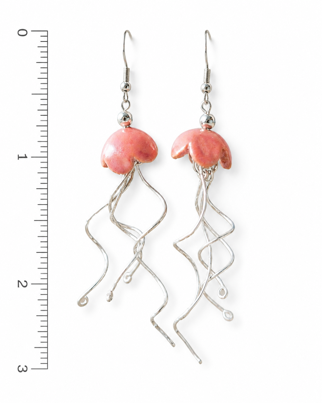 Pink ceramic jellyfish shaped earrings with long silver wire tentacles, shown next to a ruler.